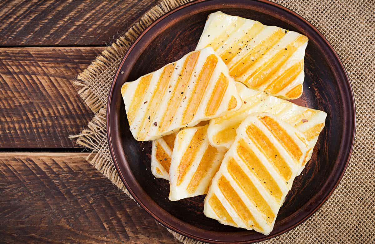 Traditional grilled halloumi cheese on plate on wooden background. Top view, above