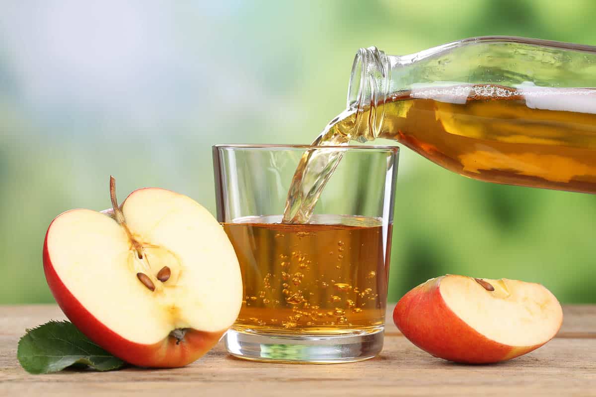 Apple juice pouring from red apples into a glass.