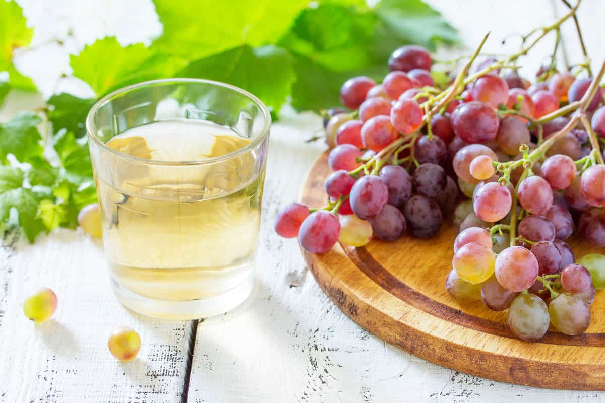 A glass of sweet grape juice, freshly squeezed, a bunch of fresh grapes on a white wooden table.