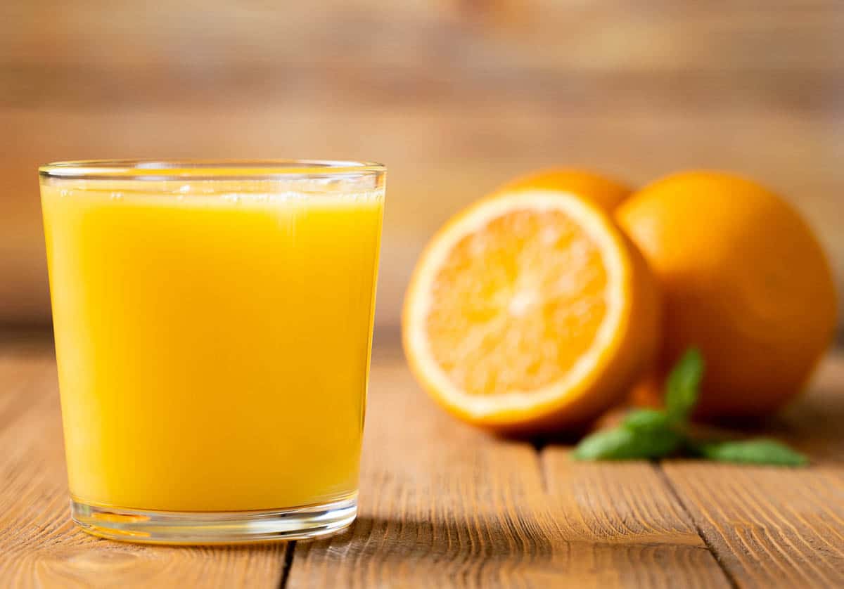 Orange Juice in a Glass with cut orange in background.