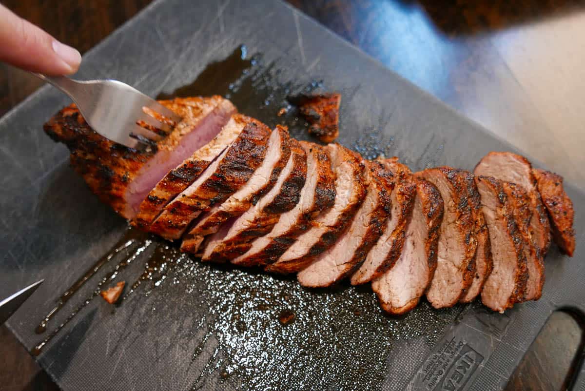 Grilled pork tenderloin, sliced, on a black cutting board.