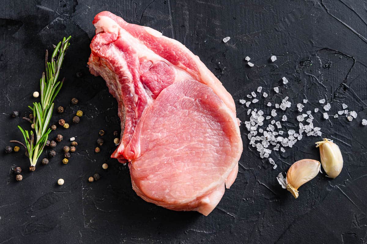 Raw pork chop on a bone with spices and rosemary and red pepper.