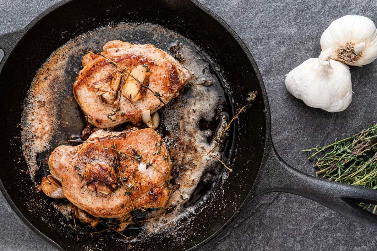 Pan Fried Pork Chops with Thyme, Garlic and Butter in a cast iron skillet.