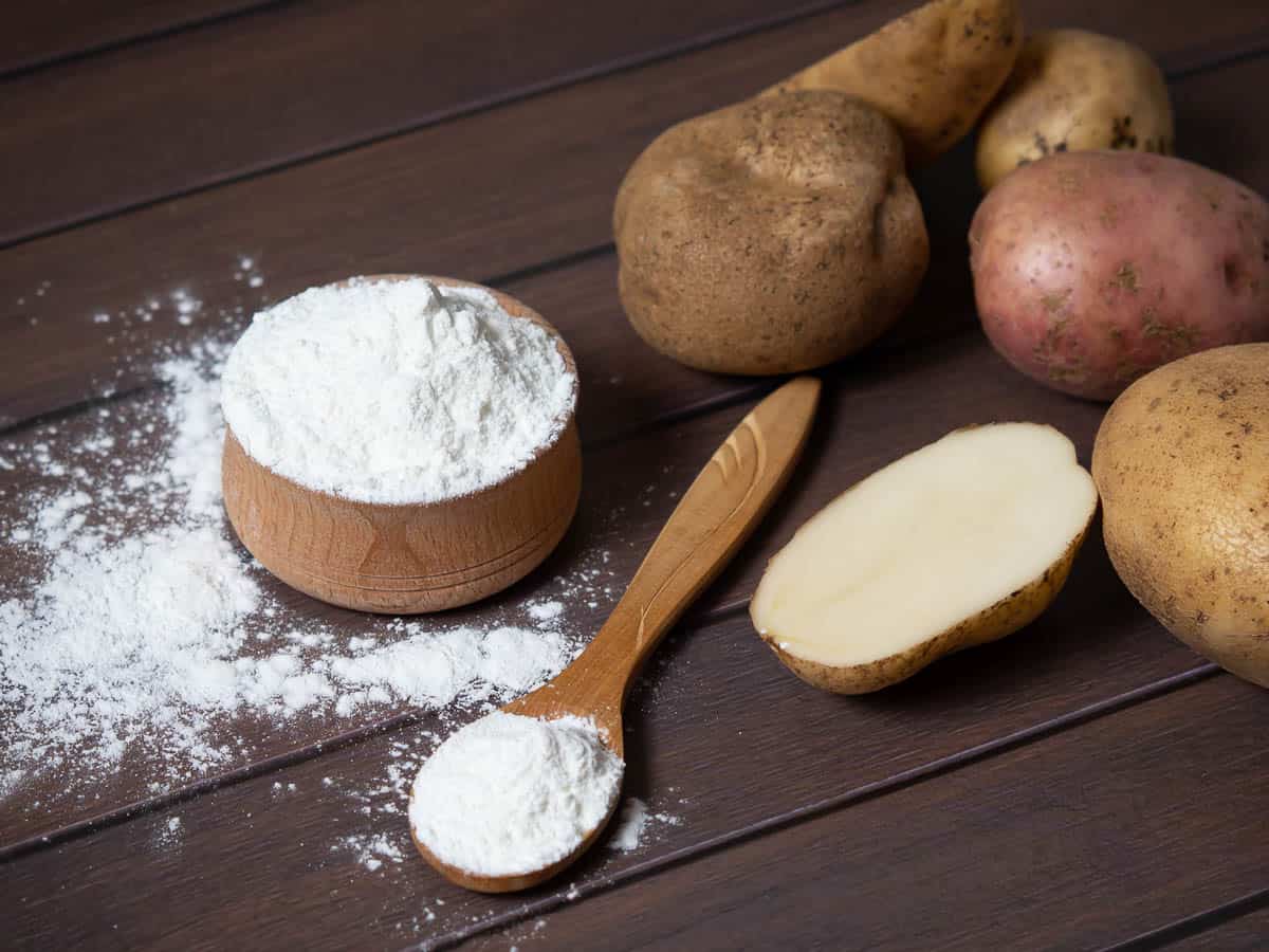 Potato starch with potatoes on a dark wooden background.