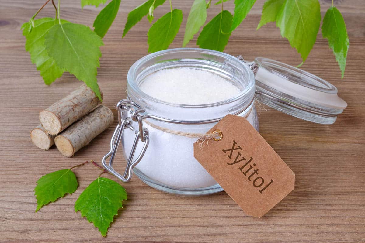 sugar substitute xylitol, a glass jar with birch sugar, liefs and wood on wooden background.