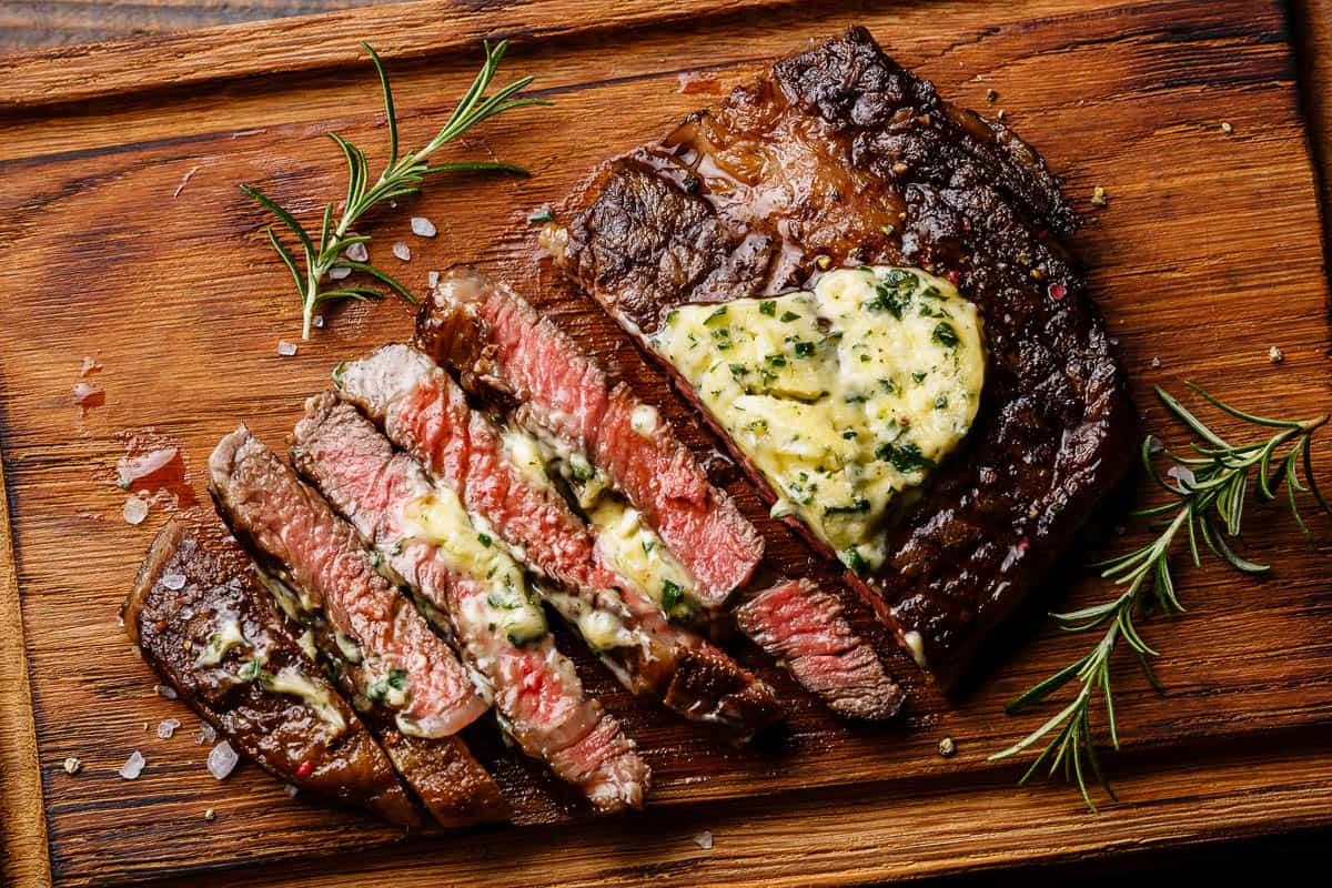 Sliced grilled Medium rare barbecue steak Ribeye with herb butter on cutting board close up.