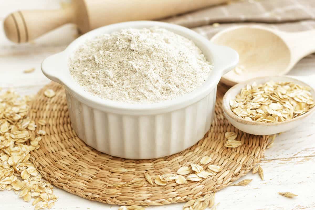 Oat flour in dish with whole oats on side.