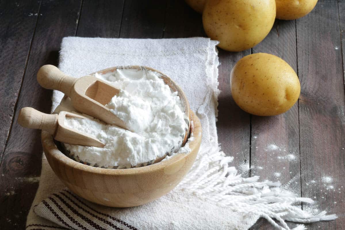 Potato starch and potatoes on wooden background.