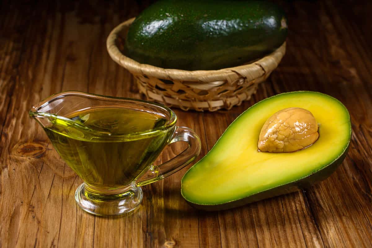 Half avocado and avocado oil in a glass bowl on rustic table.