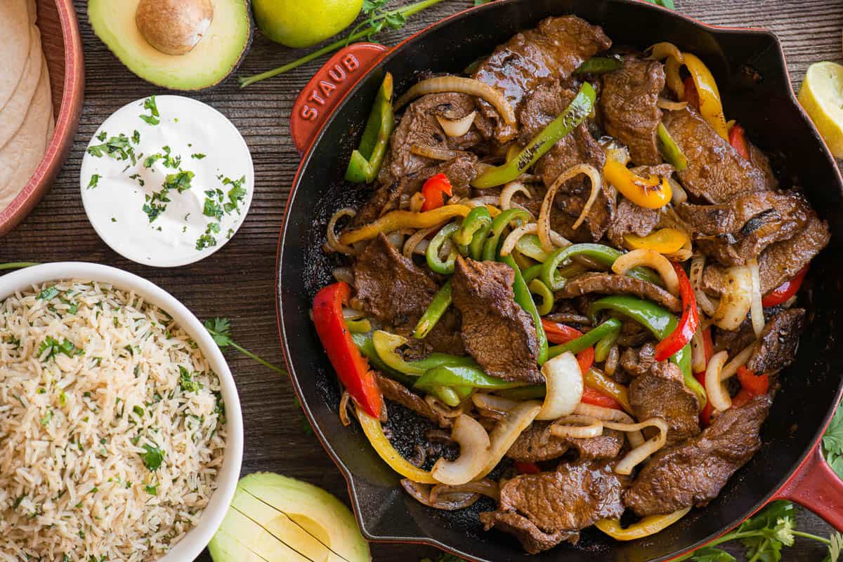 large skillet of steak fajitas with peppers and onions.