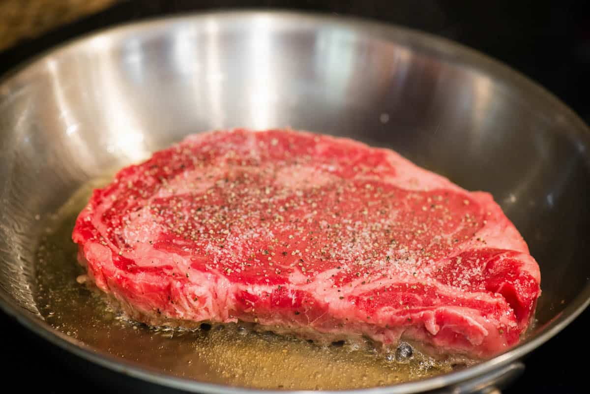 raw ribeye in skillet with oil.