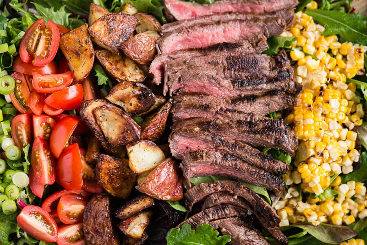 steak salad with sliced steak, corn, potatoes, and greens.