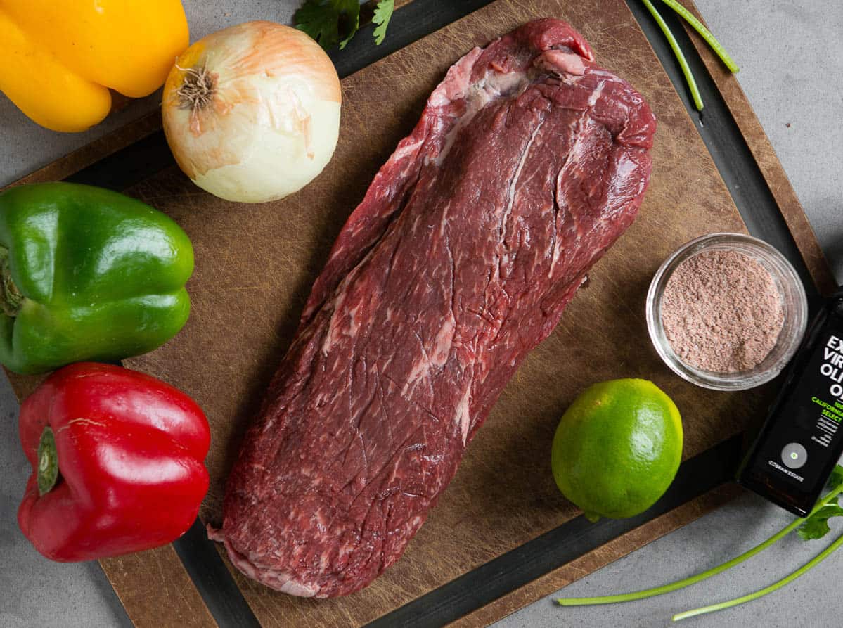 raw skirt steak on cutting board with onion and peppers.