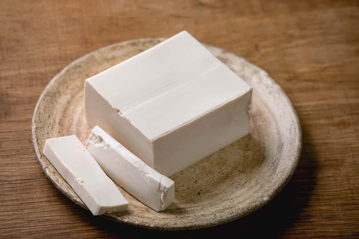 Silk tofu japanese soy cheese whole piece on ceramic plate with chopsticks over wooden table.