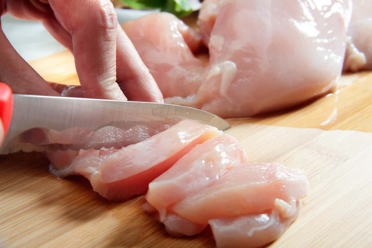 Man's hand cutting raw chicken breast.