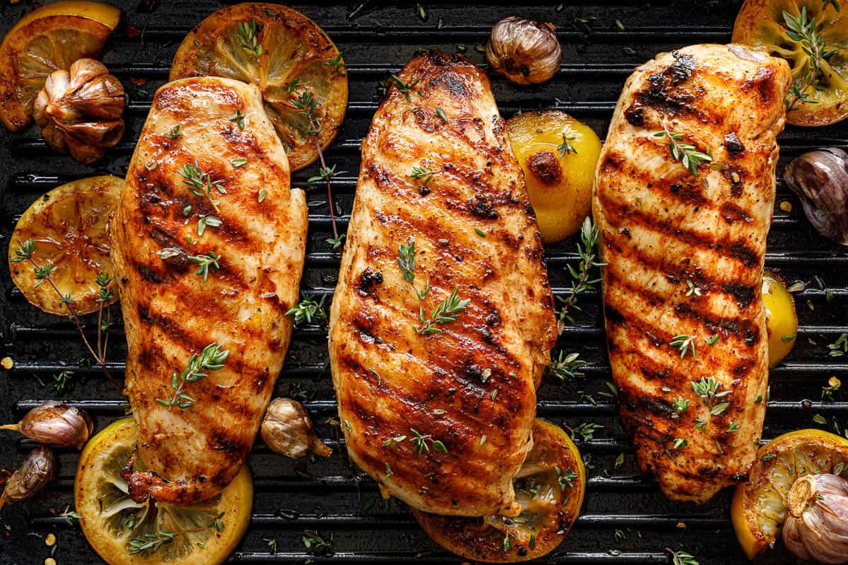 Grilled chicken breasts with thyme, garlic and lemon slices on a grill pan.