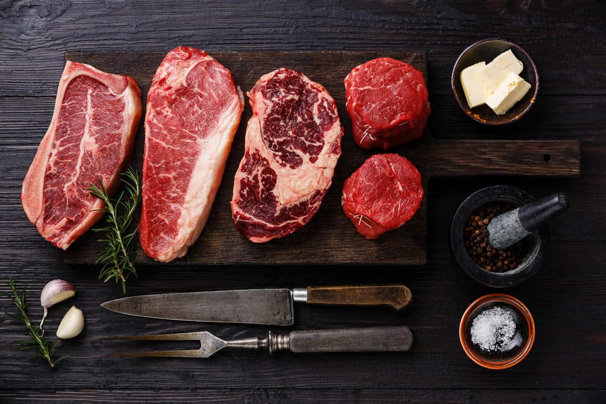 Variety of Raw Black Angus Prime meat steaks Blade on bone, Striploin, Rib eye, Tenderloin fillet mignon on wooden board and seasoning.