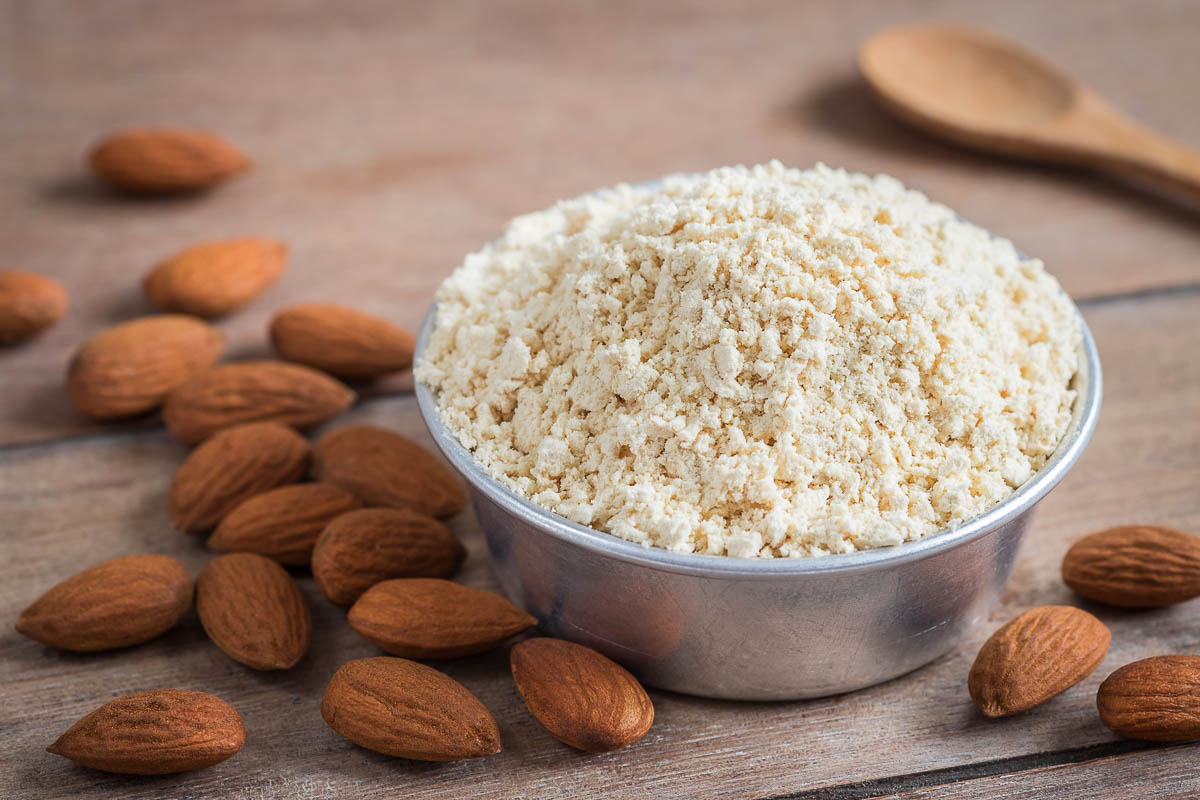 Almond flour in bowl and almonds on wooden table.