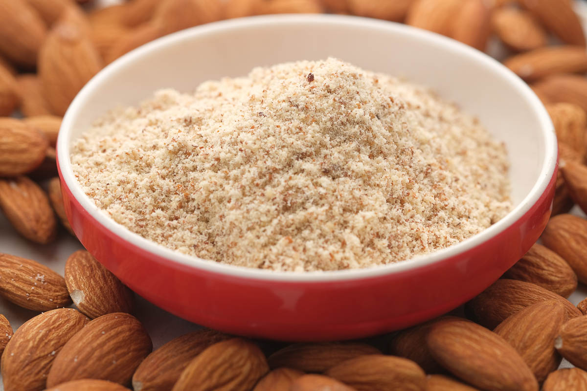 almond powder in a container with almond nut on table.