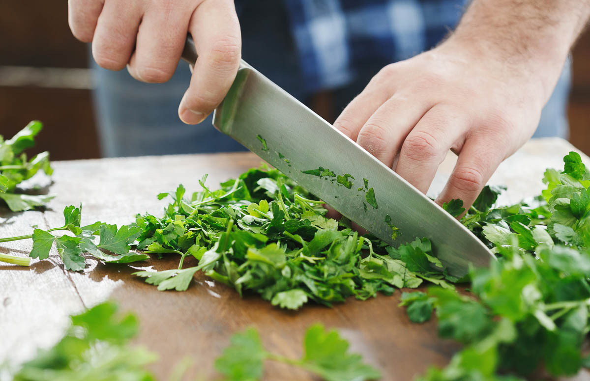 Man is chopping cilantro or parsley.