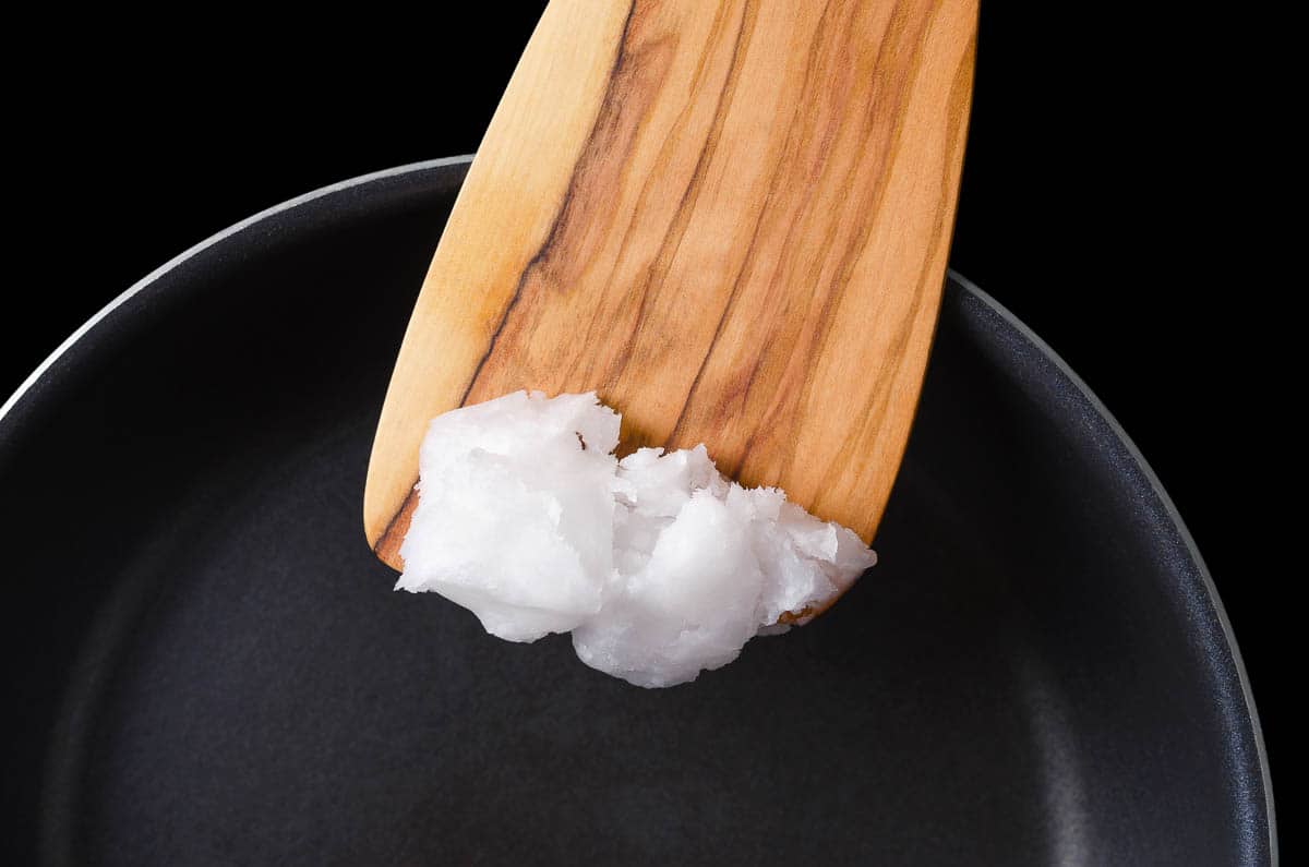 Coconut oil on wooden spatula over coated pan.