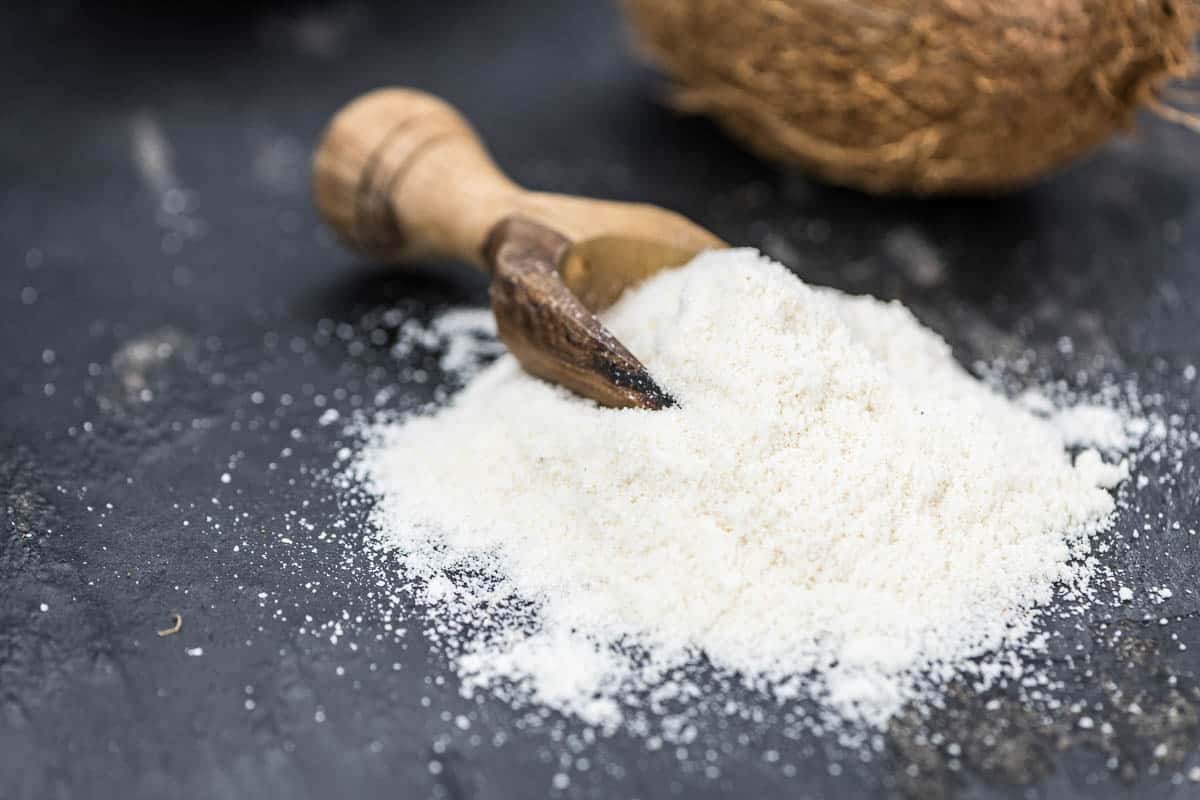 coconut flour in scoop next to out of focus coconut.