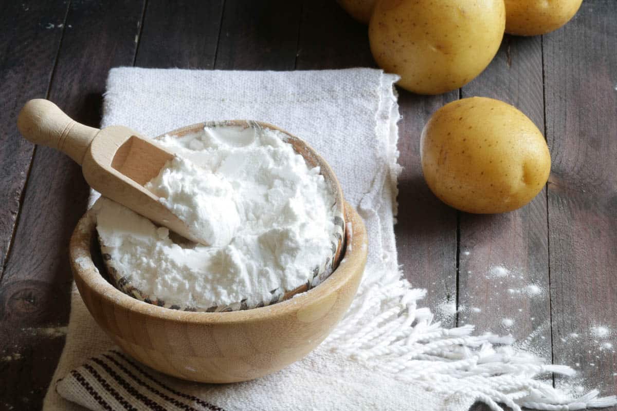 Potato starch and potatoes on wooden background.