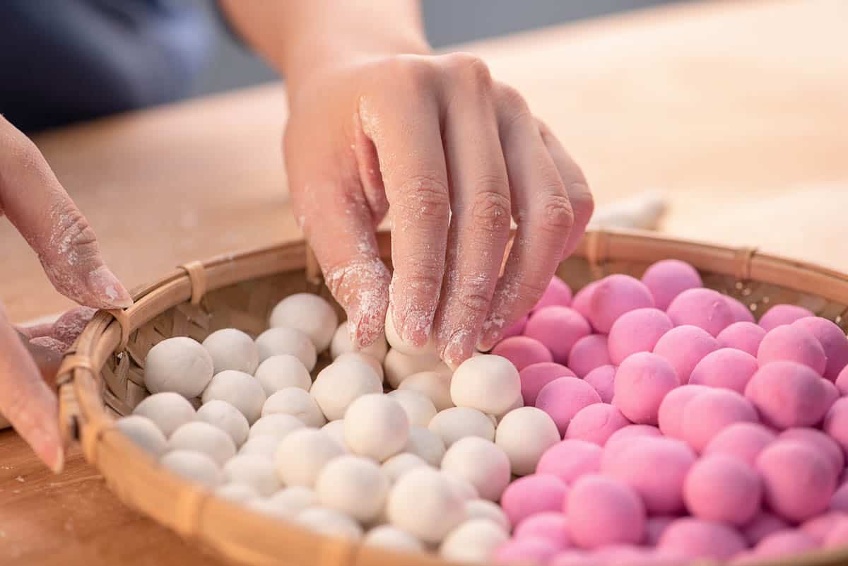 A woman is making Tang yuan, yuan xiao, Chinese traditional food rice dumplings in red and white for lunar new year, winter festival, close up.