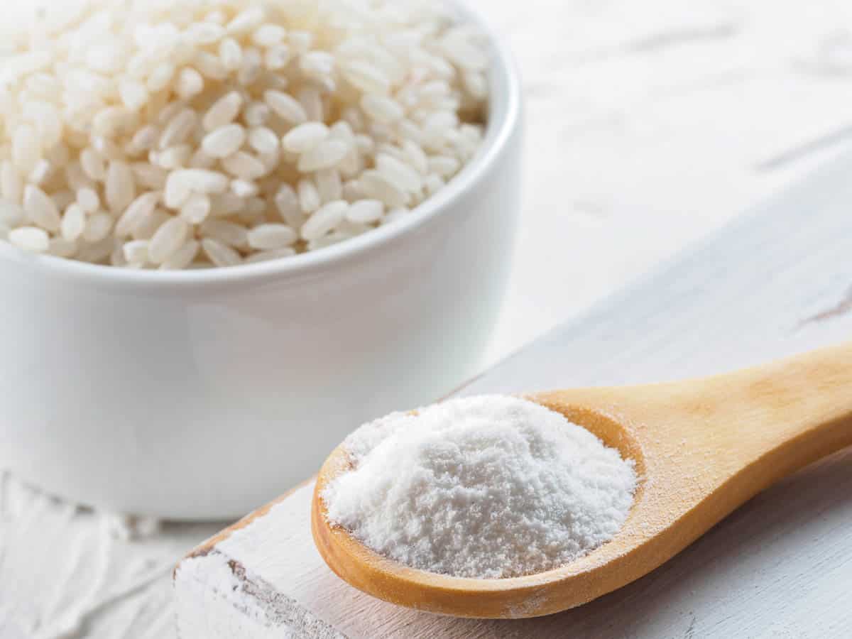 rice flour in wooden spoon and rice grains on white background.