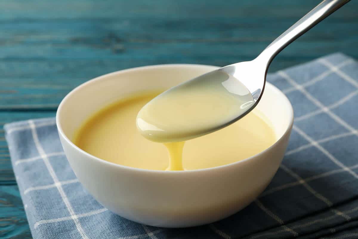 Towel, spoon and bowl with condensed milk on wooden background.