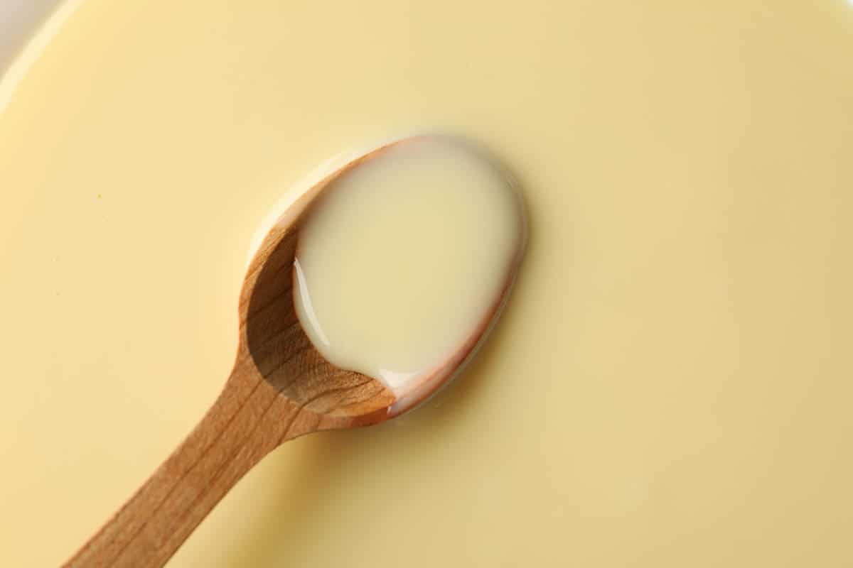 Wooden spoon in condensed milk, close up.