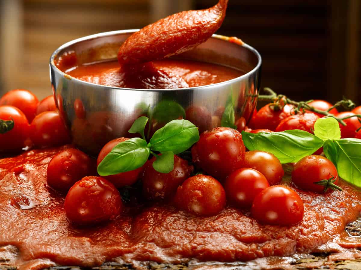 homemade tomato puree in bowl, also spilled over onto table, with fresh tomatoes.