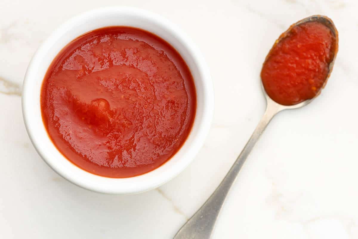 Fresh tomato sauce on bowl and spoon on white marble table.