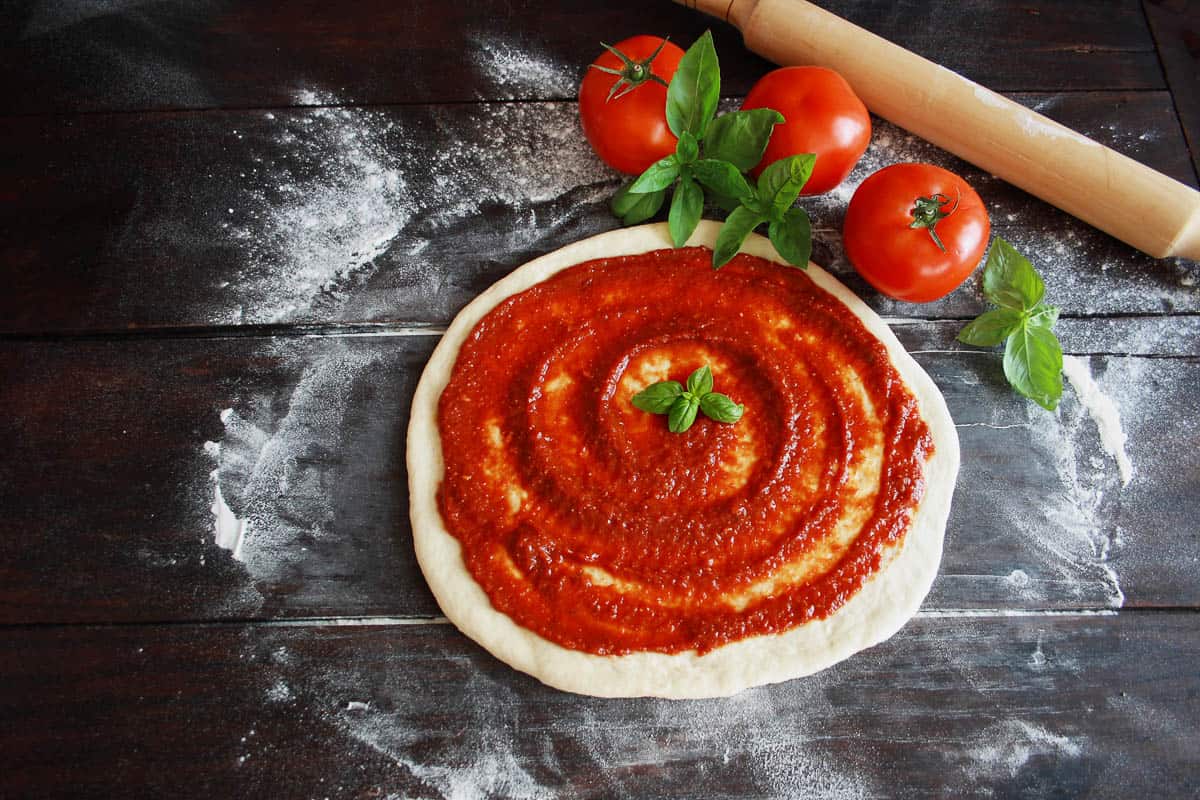 Raw pizza dough with tomato sauce and basil leaves.