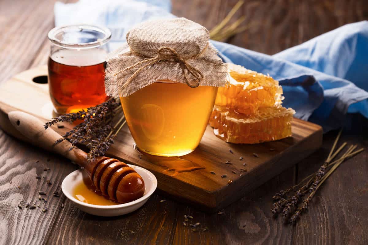 Jar of liquid honey with honeycomb on side.
