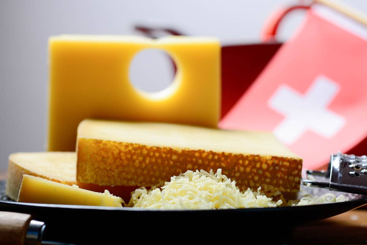 Assortment of Swiss cheeses Emmental or Emmentaler medium-hard cheese with round holes, Gruyere, appenzeller and raclette used for traditional cheese fondue and gratin and flag of Switzerland.