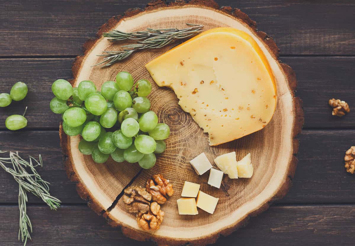 Cheese platter, gouda herb on natural wood disc with grapes and nuts.